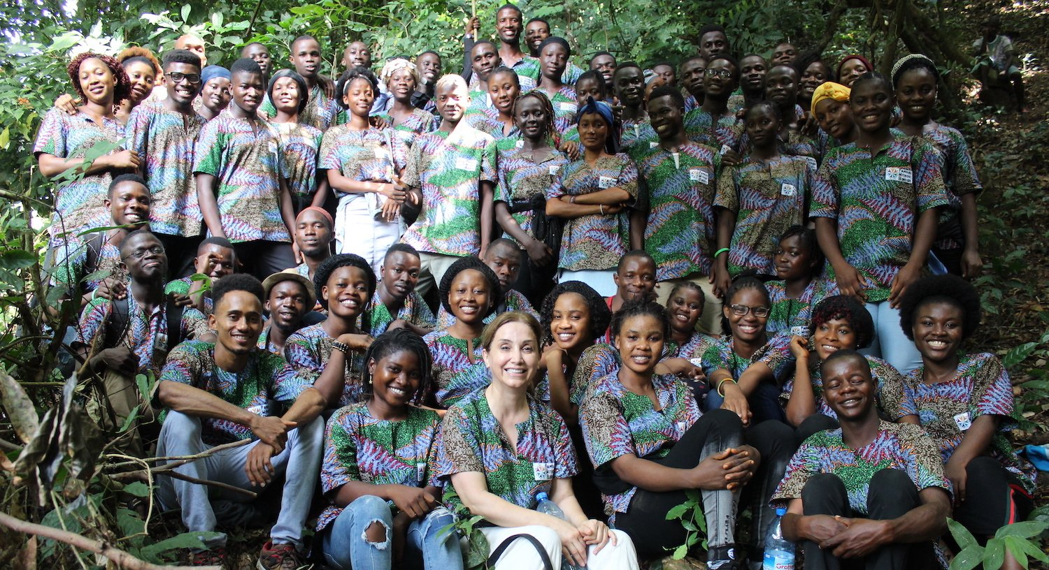 A large group of people are posing for a picture in the woods.