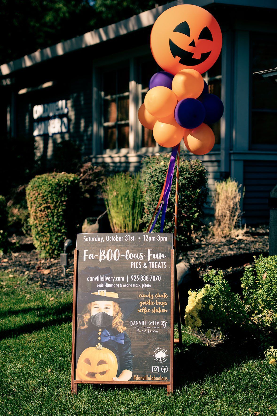 A sign with a pumpkin and balloons on it in front of a house.