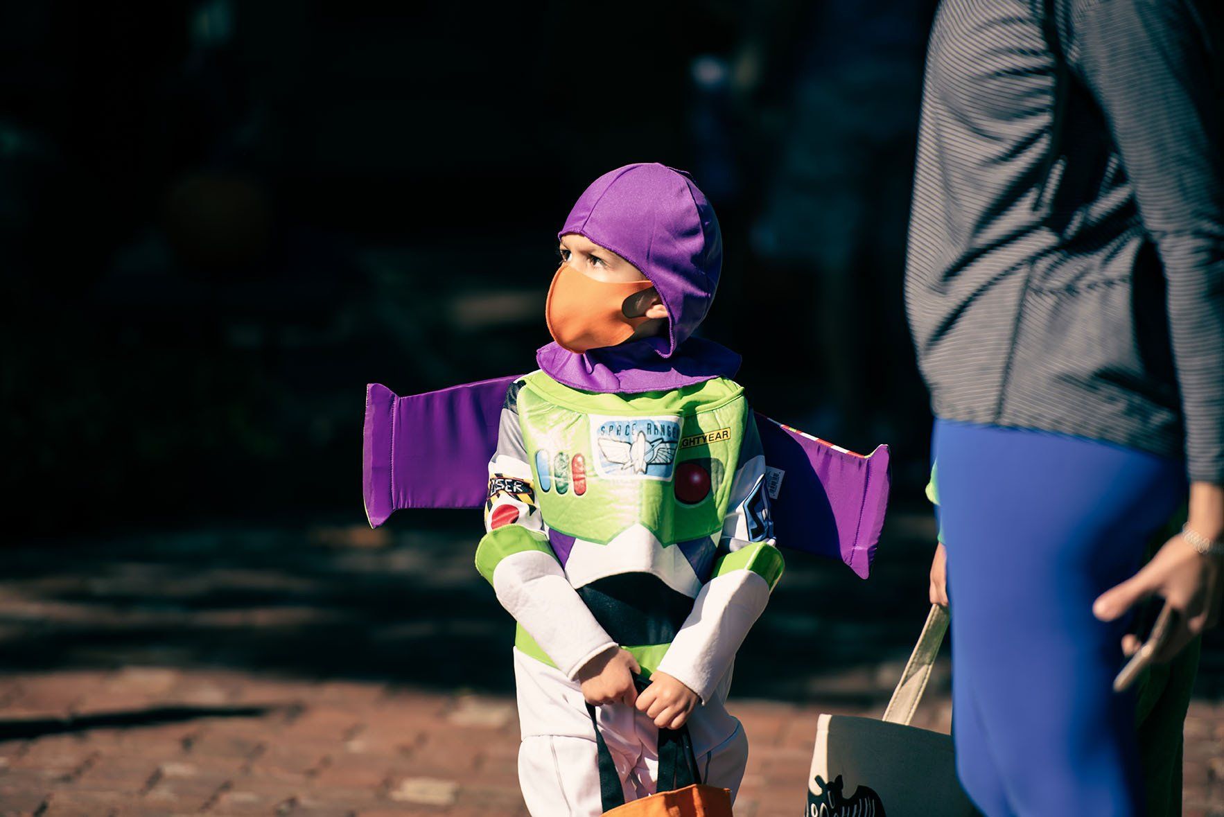A little boy dressed as buzz lightyear from toy story is standing next to a woman.