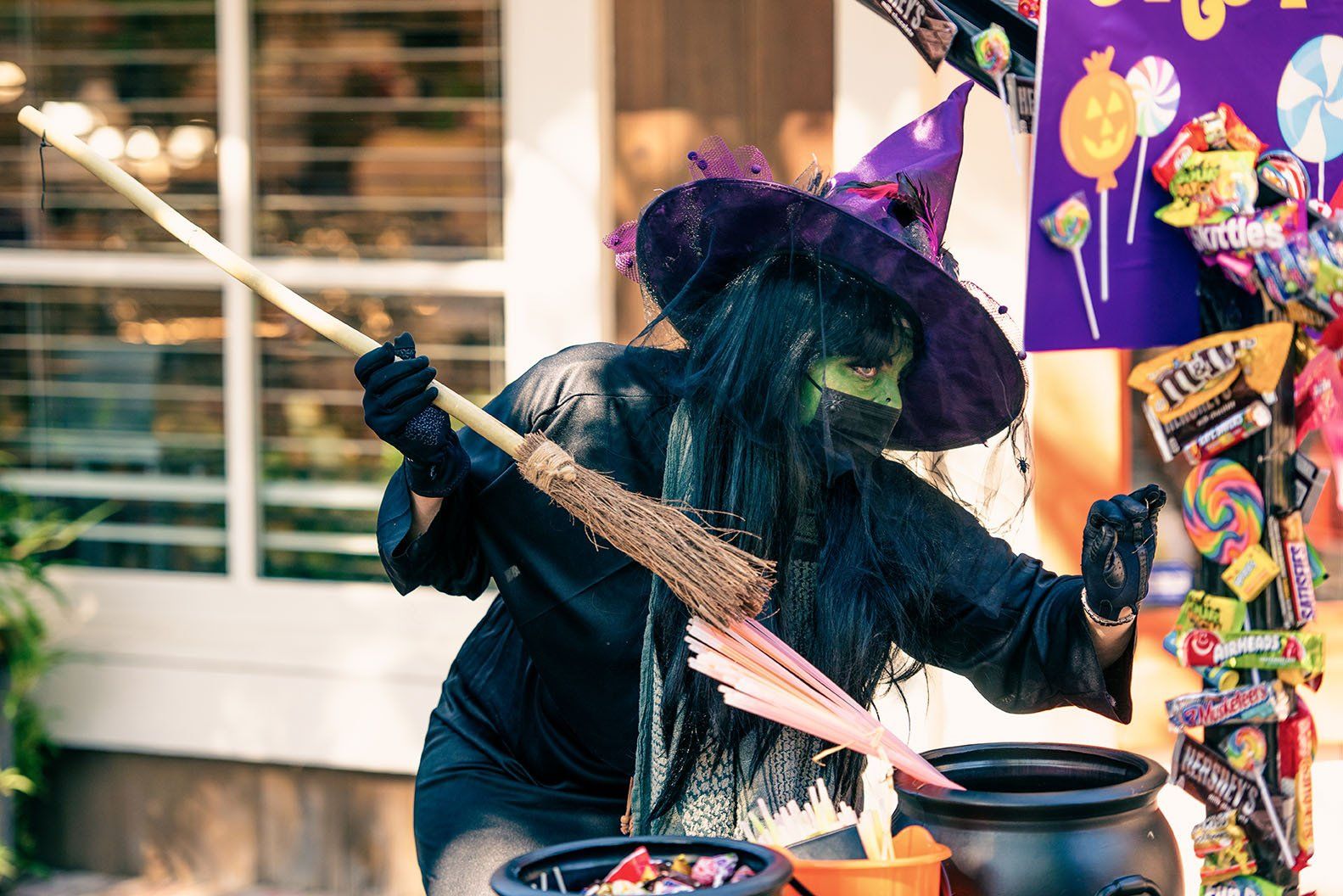 A woman dressed as a witch is pouring candy into a cauldron.