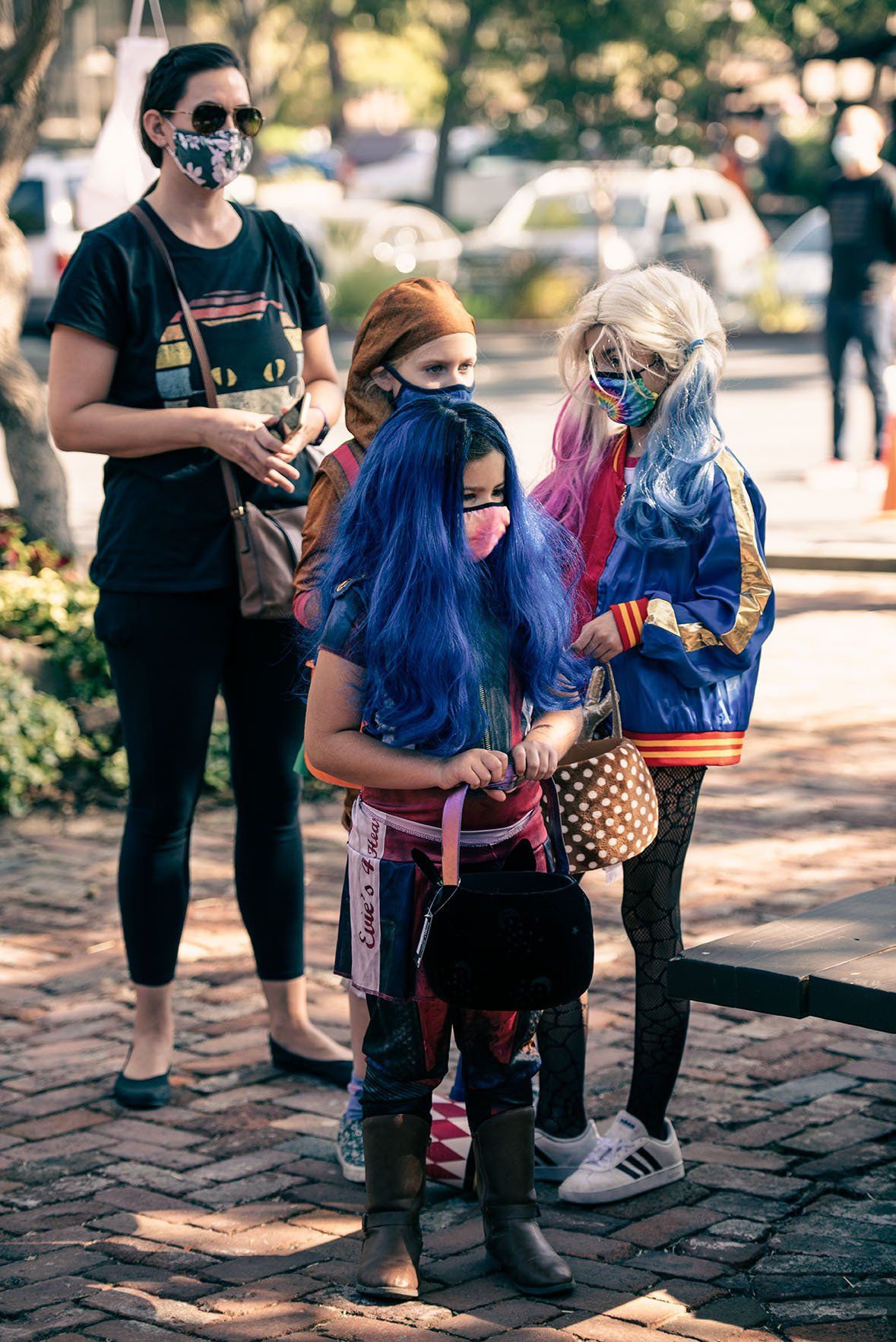 A group of children wearing masks and costumes are standing next to each other on a sidewalk.