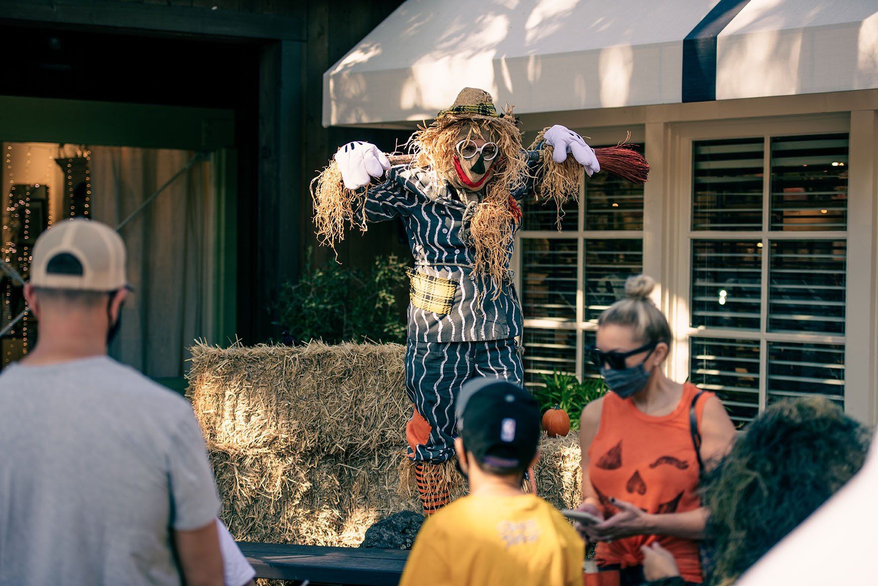 A scarecrow is standing in front of a building with people looking at it.