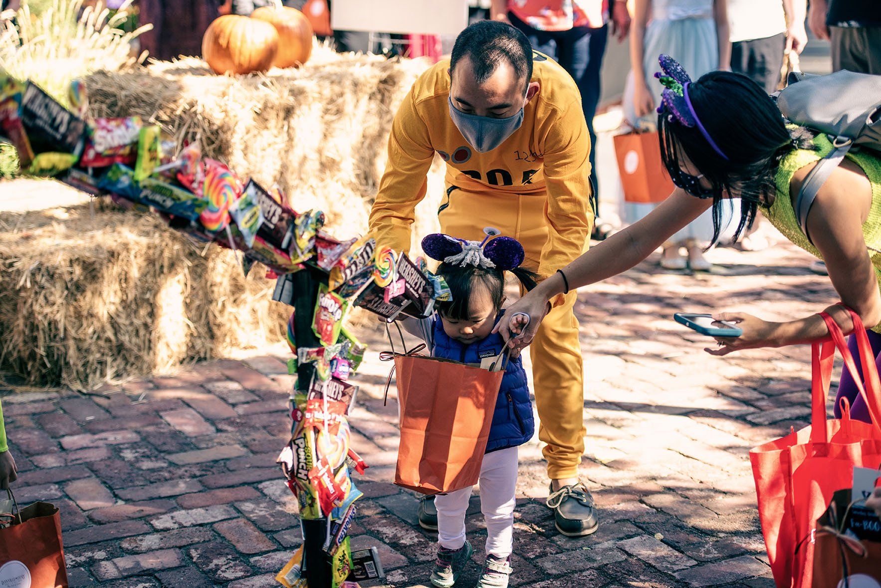 A man and a woman are holding the hand of a little girl in a halloween costume.