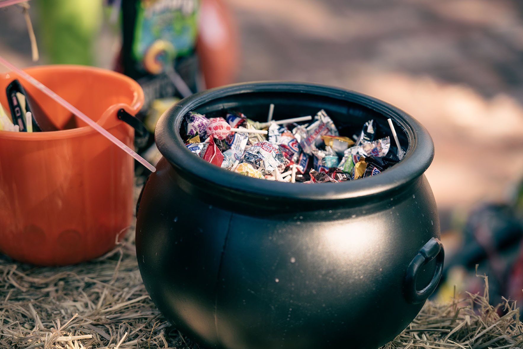 A cauldron filled with candy is sitting on a pile of hay.