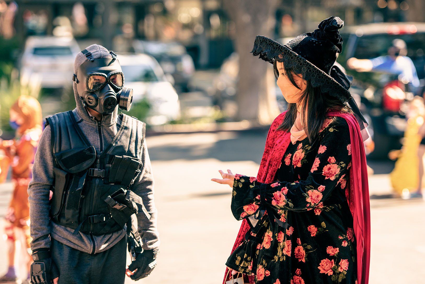 A man in a gas mask is talking to a woman in a witch costume.