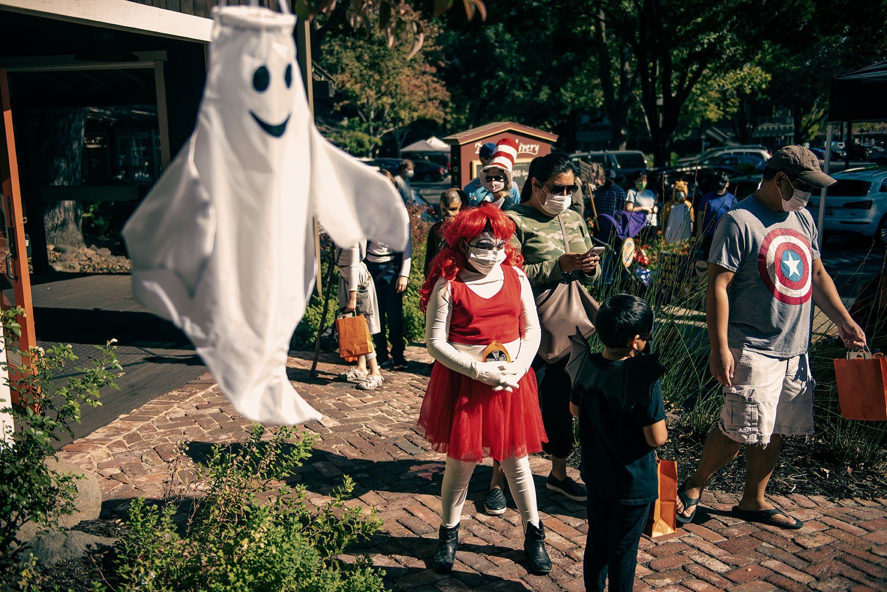 A group of people dressed in halloween costumes are walking down a brick sidewalk.