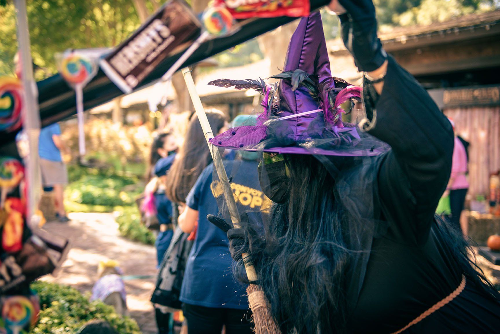 A woman dressed as a witch is holding a broom and candy.