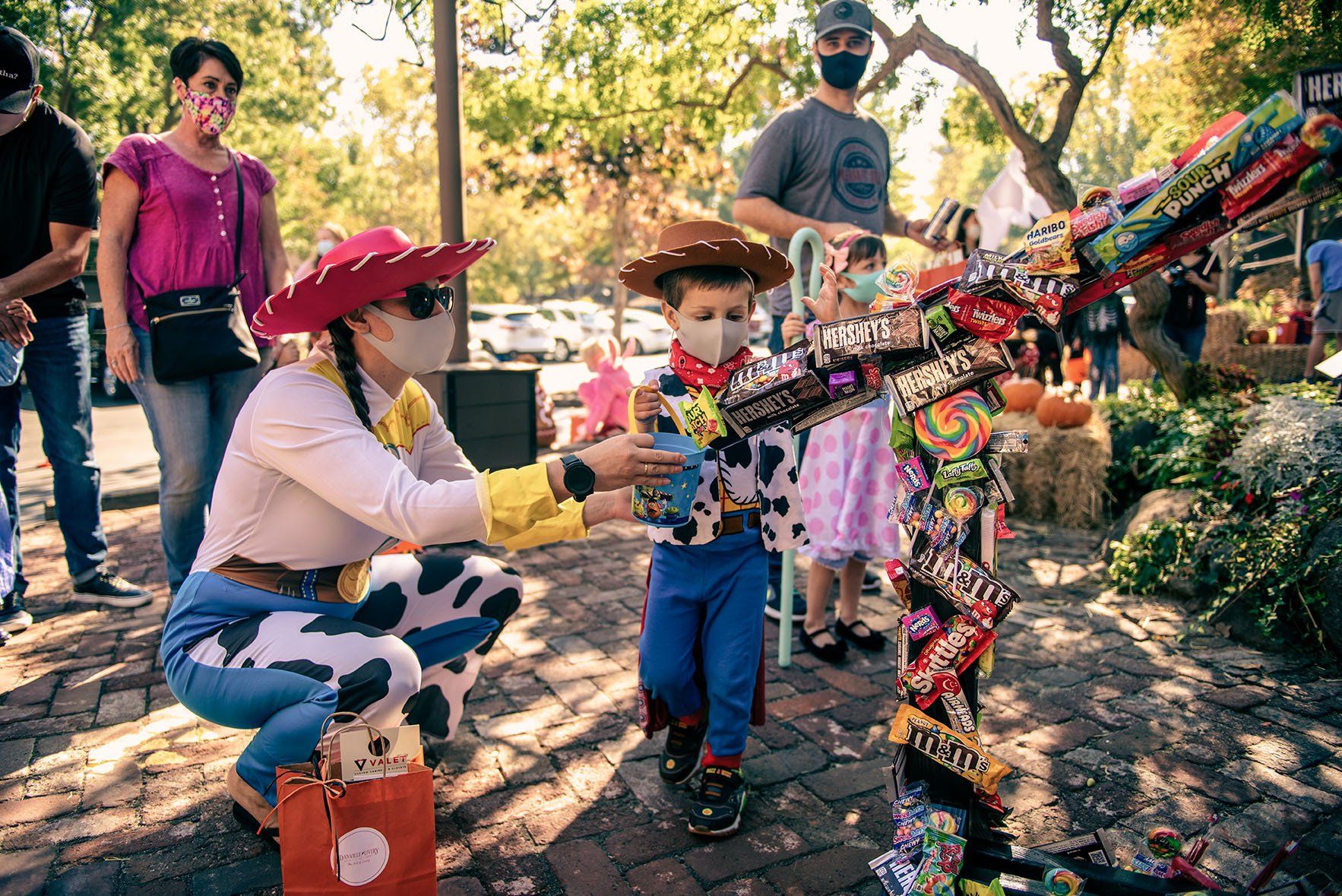 A woman in a cowboy hat is kneeling down next to a boy in a toy story costume.