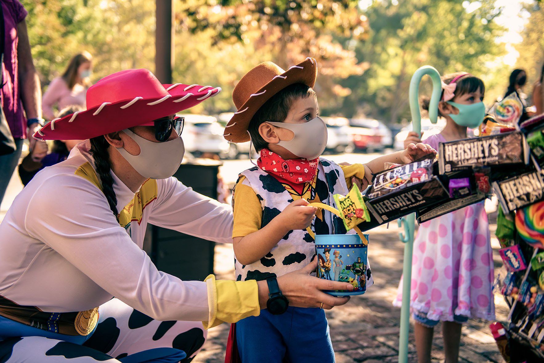 A woman in a toy story costume is giving a child a bucket of candy.