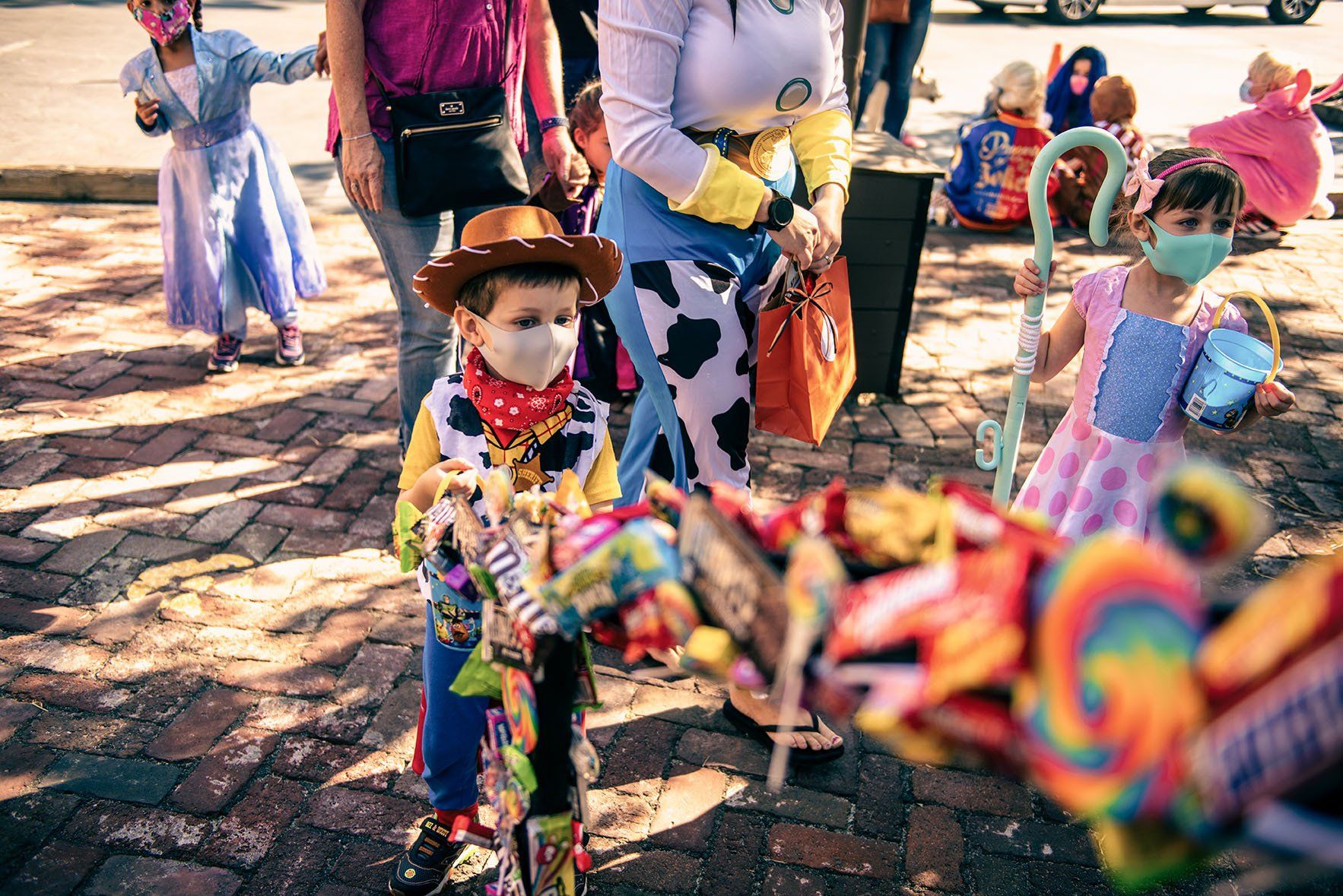 A group of children dressed in costumes are standing on a brick sidewalk.