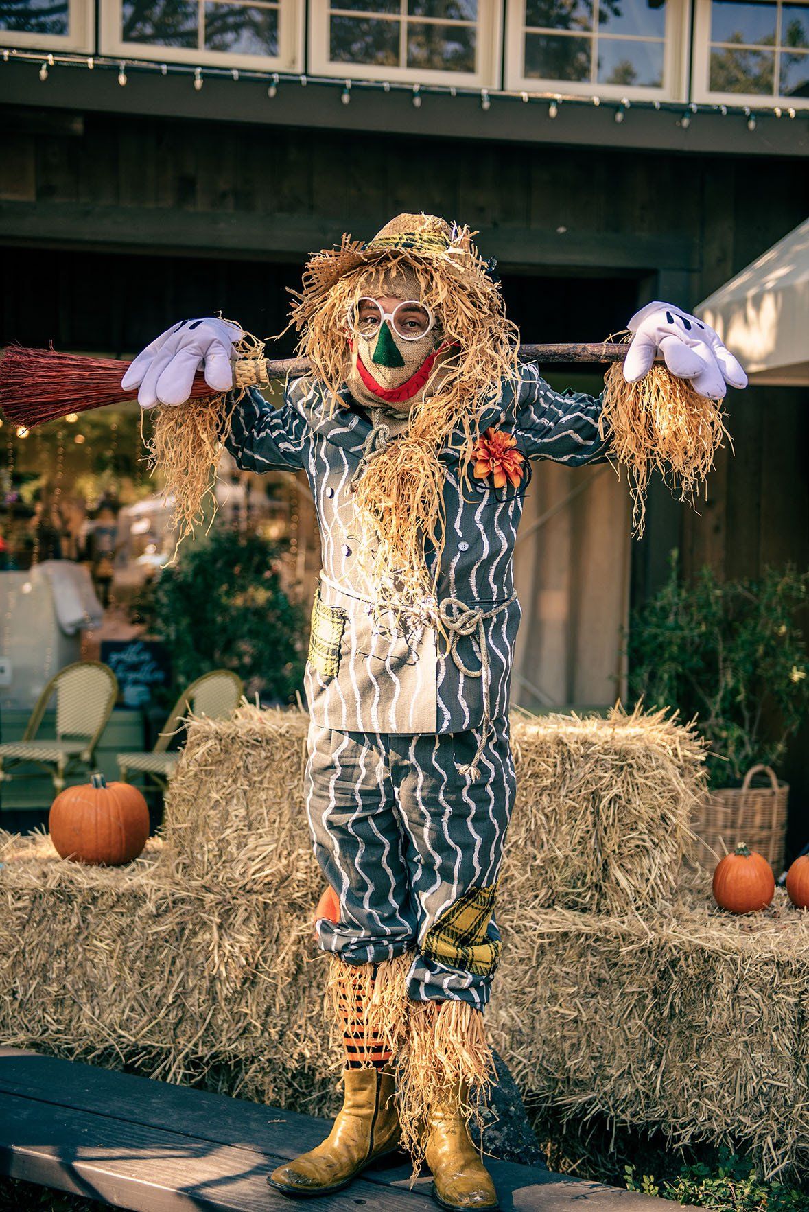 A scarecrow is standing in front of hay bales and pumpkins.