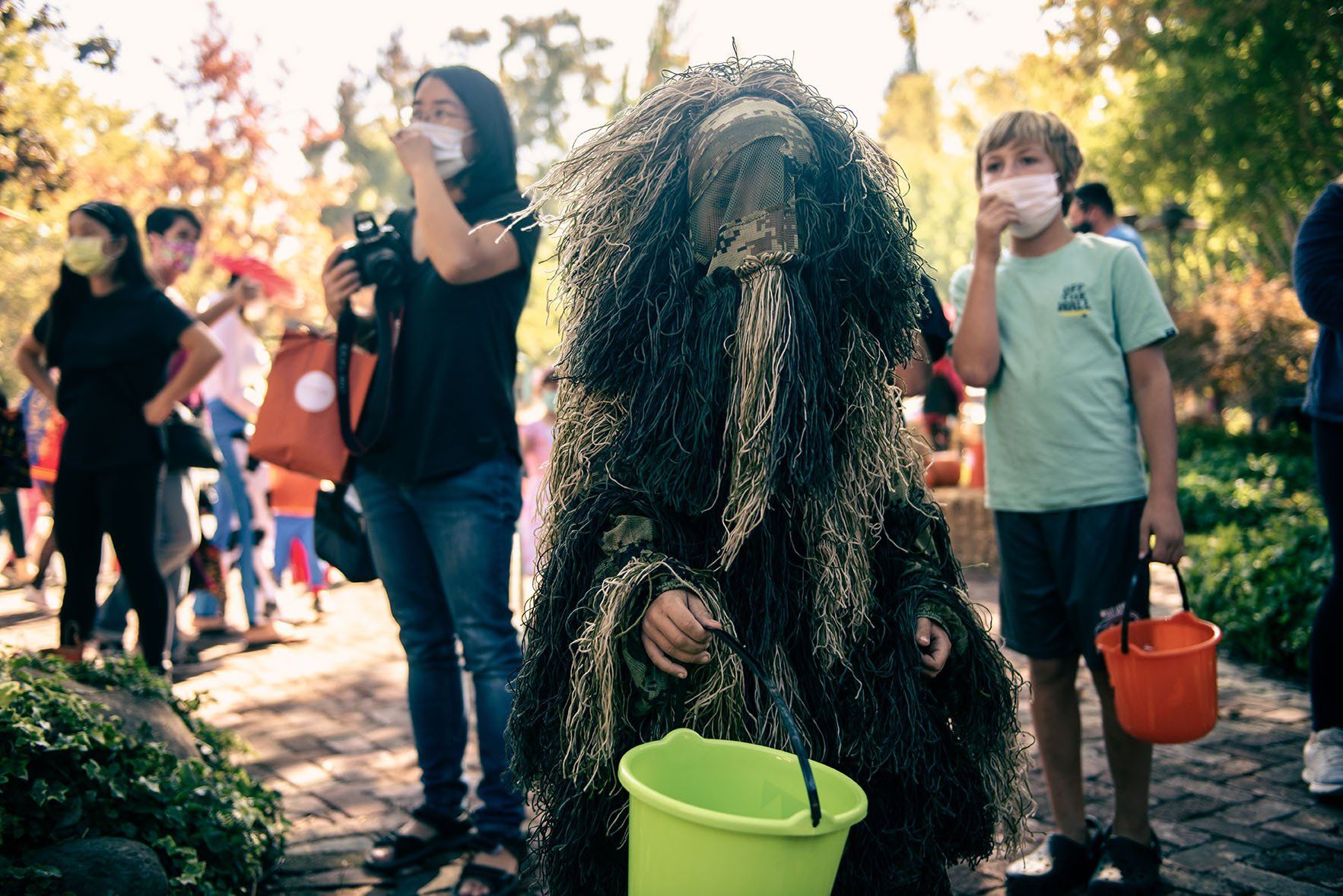 A man in a costume is holding a green bucket in front of his face.