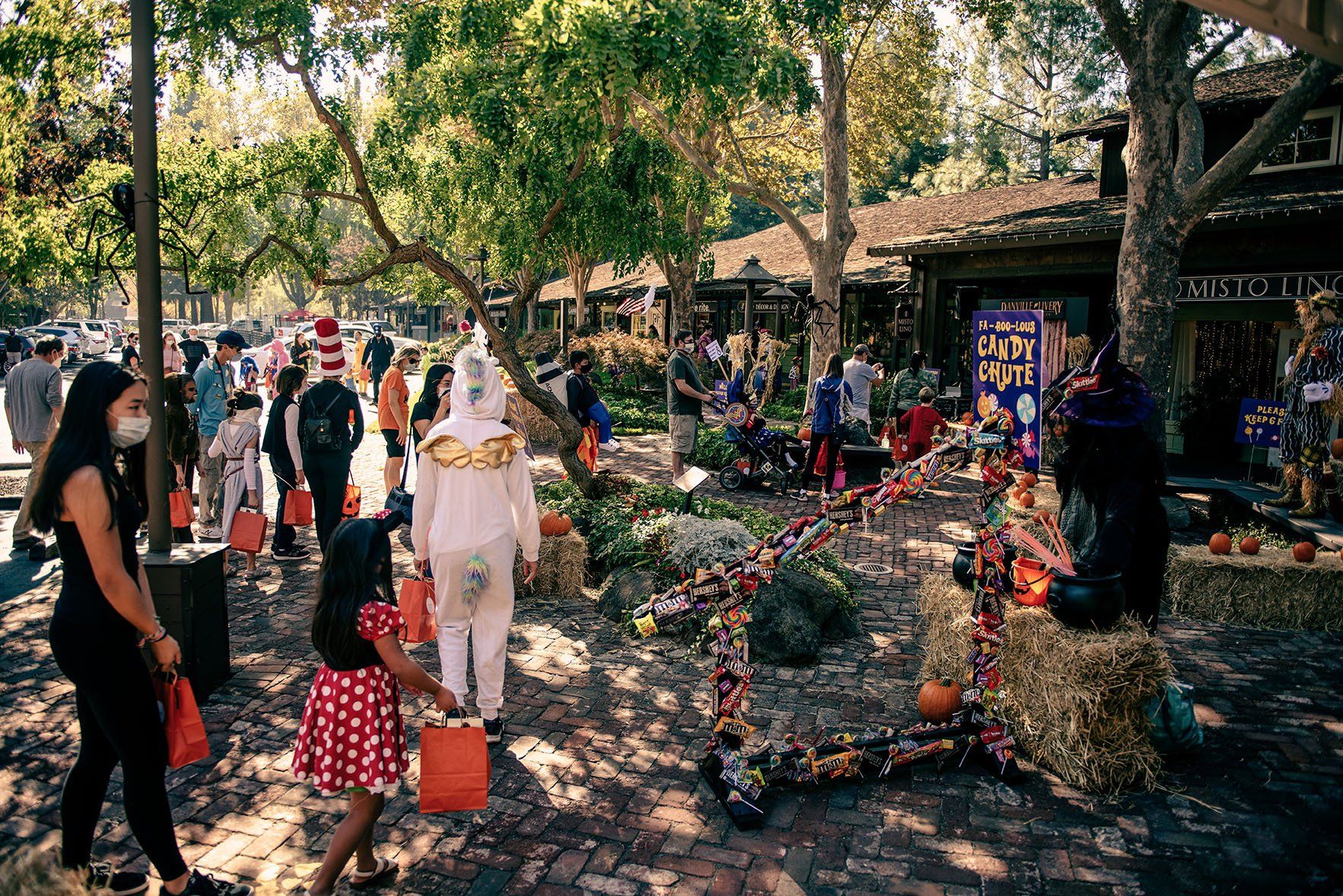 A group of people are walking down a street at a halloween trick or treat event.