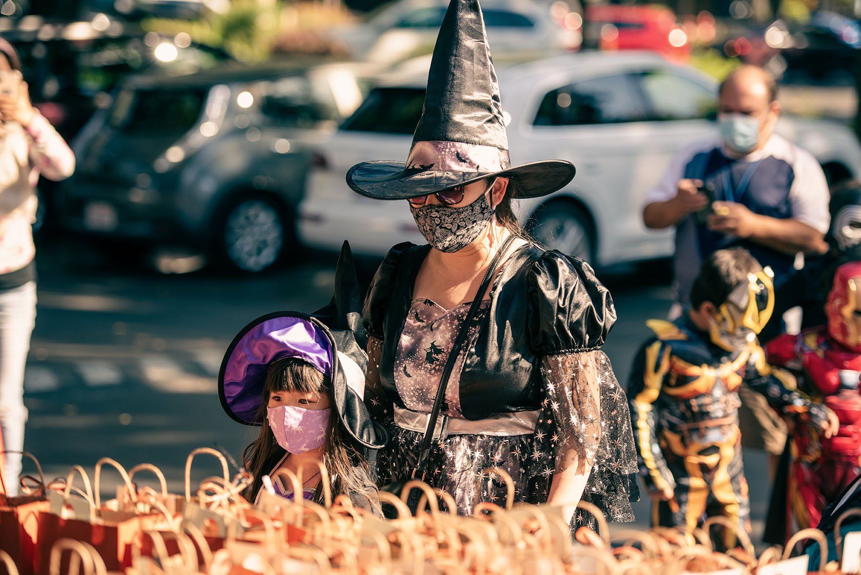 A woman in a witch costume is standing next to a girl in a skeleton costume.