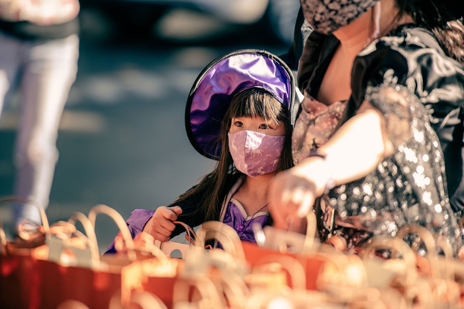 A little girl wearing a mask and a witch costume is sitting next to a woman.