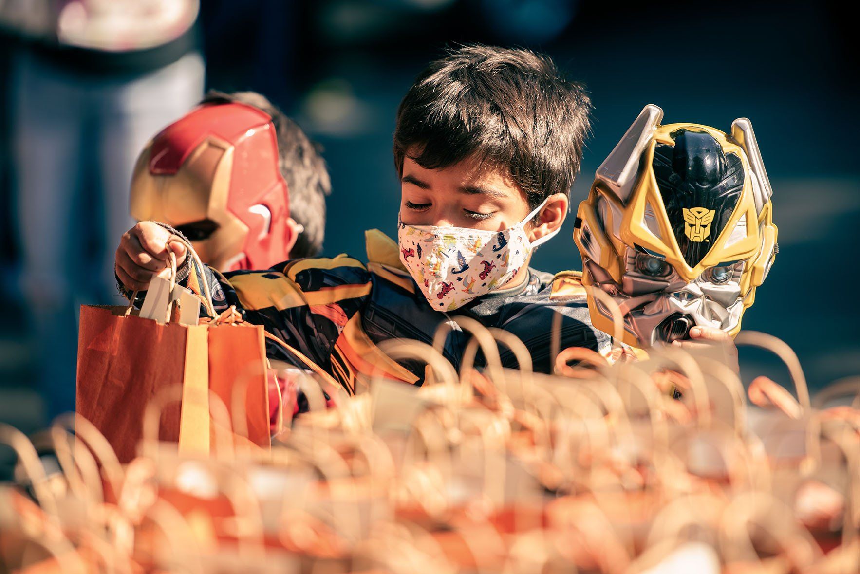 A boy wearing a mask is holding a trick or treat bag.