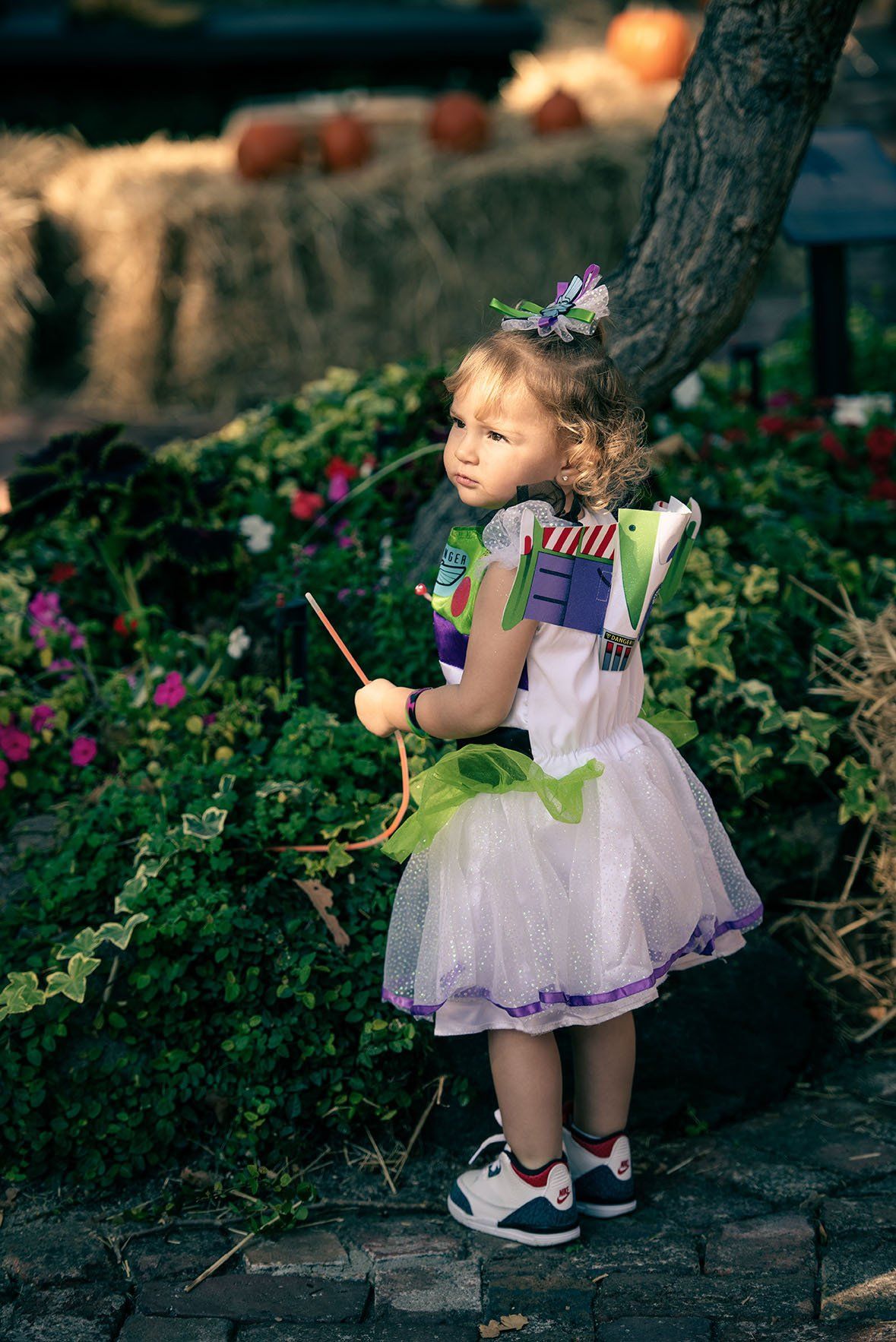 A little girl in a fairy costume is standing next to a tree holding a wand.