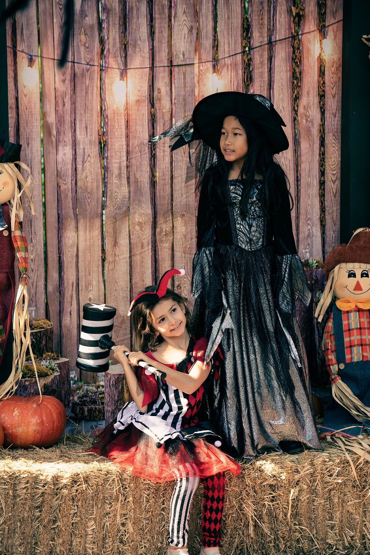 Two little girls in halloween costumes are sitting on a bale of hay.