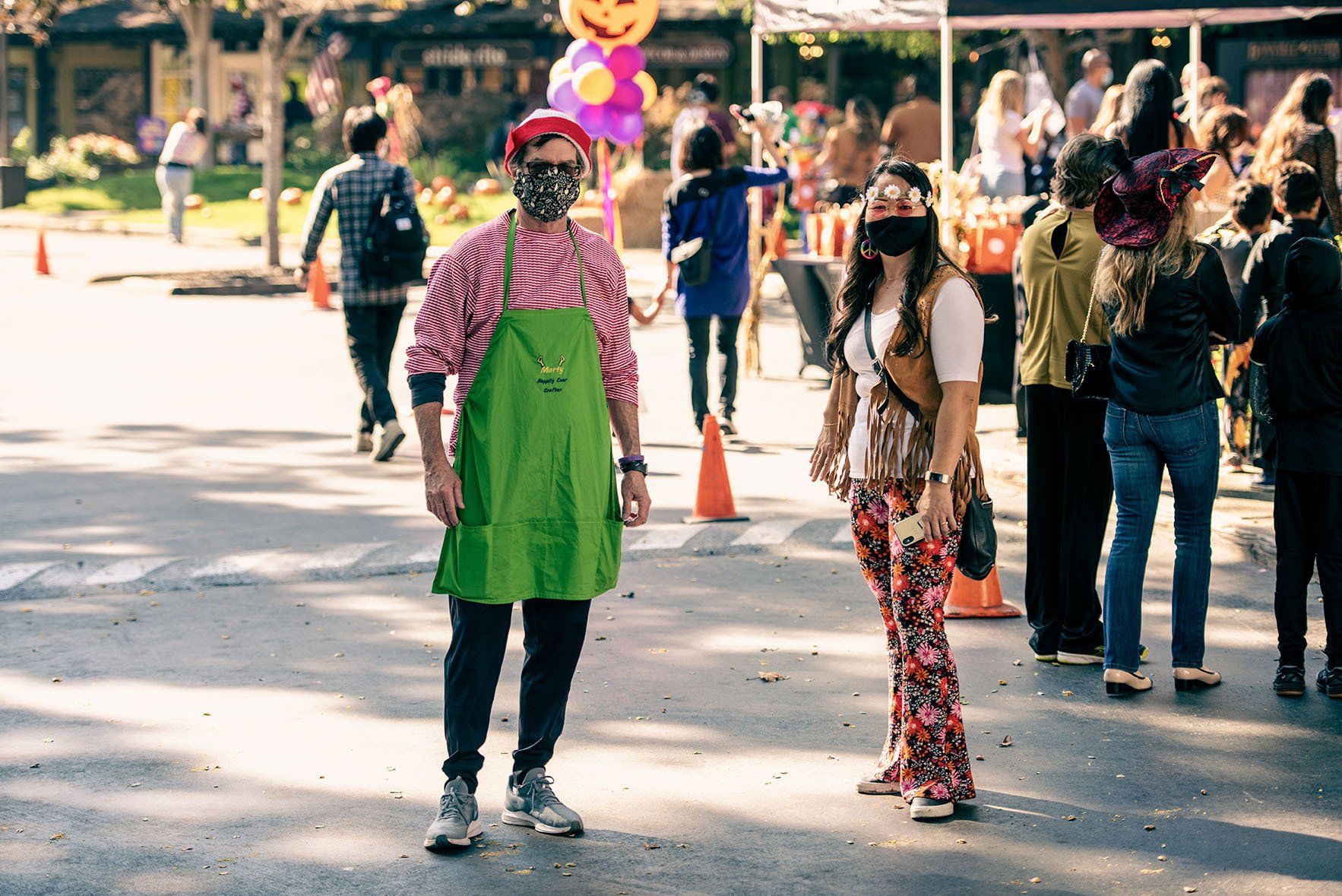 A man in a green apron is standing next to a woman wearing a mask.