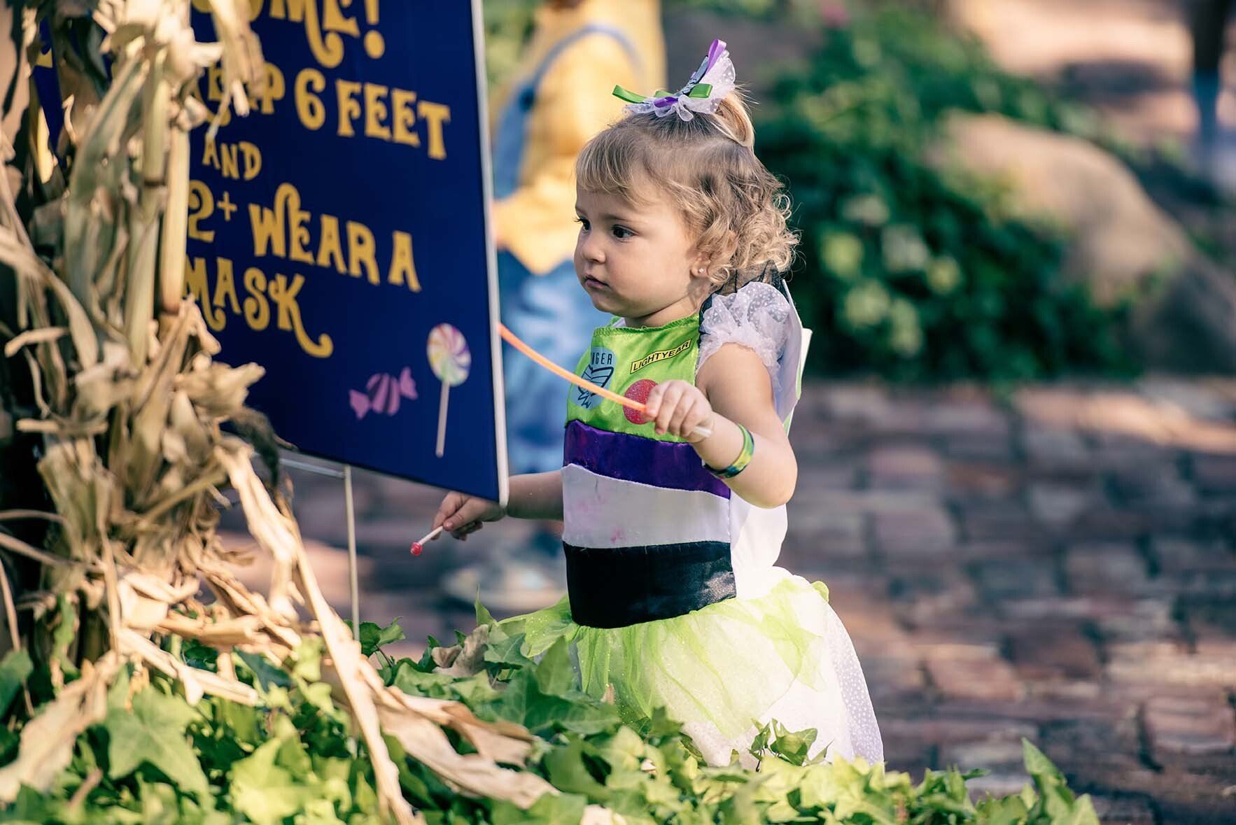 A little girl in a fairy costume is holding a sign that says wear a mask.