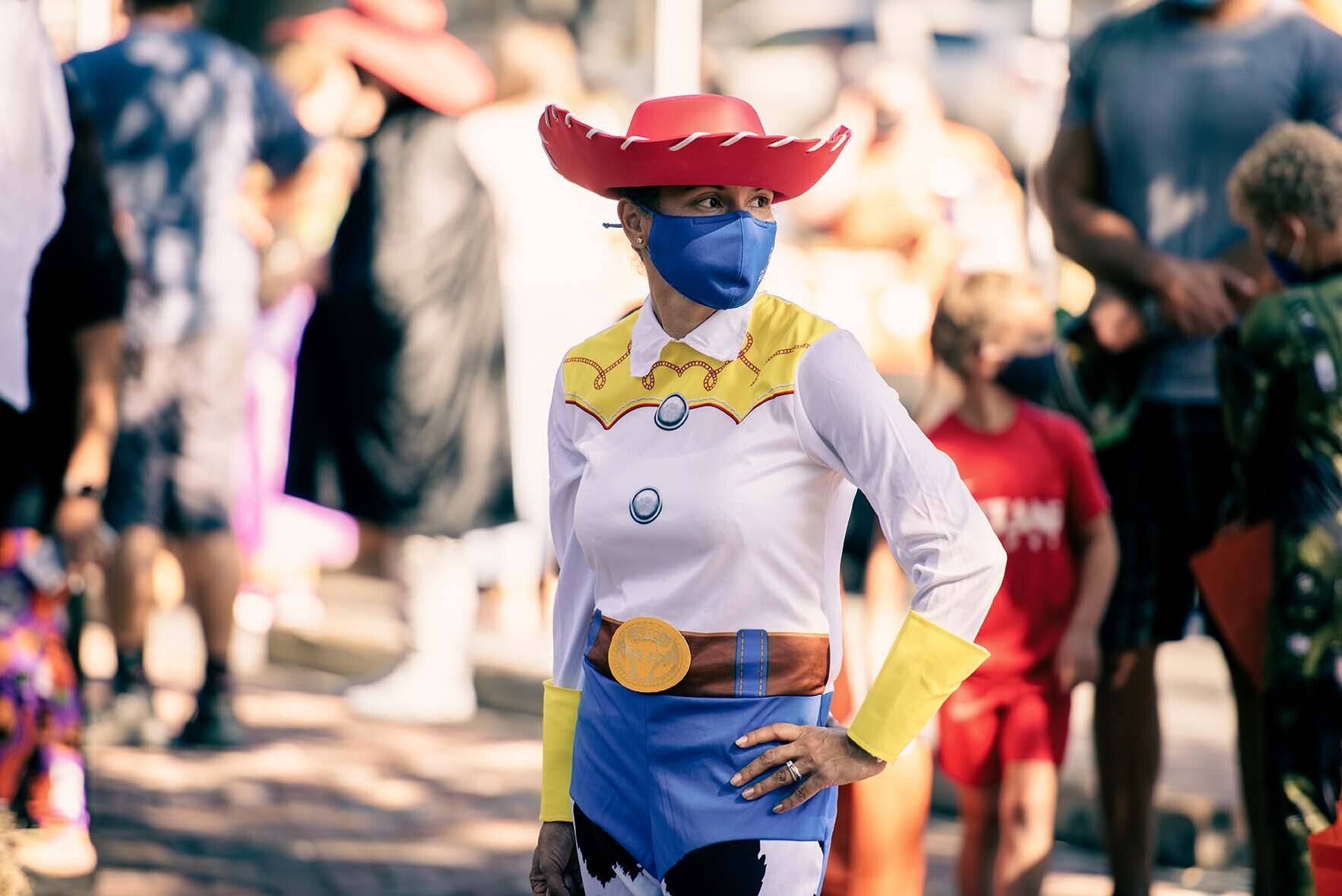 A woman wearing a mask and a cowboy costume is standing in front of a crowd.
