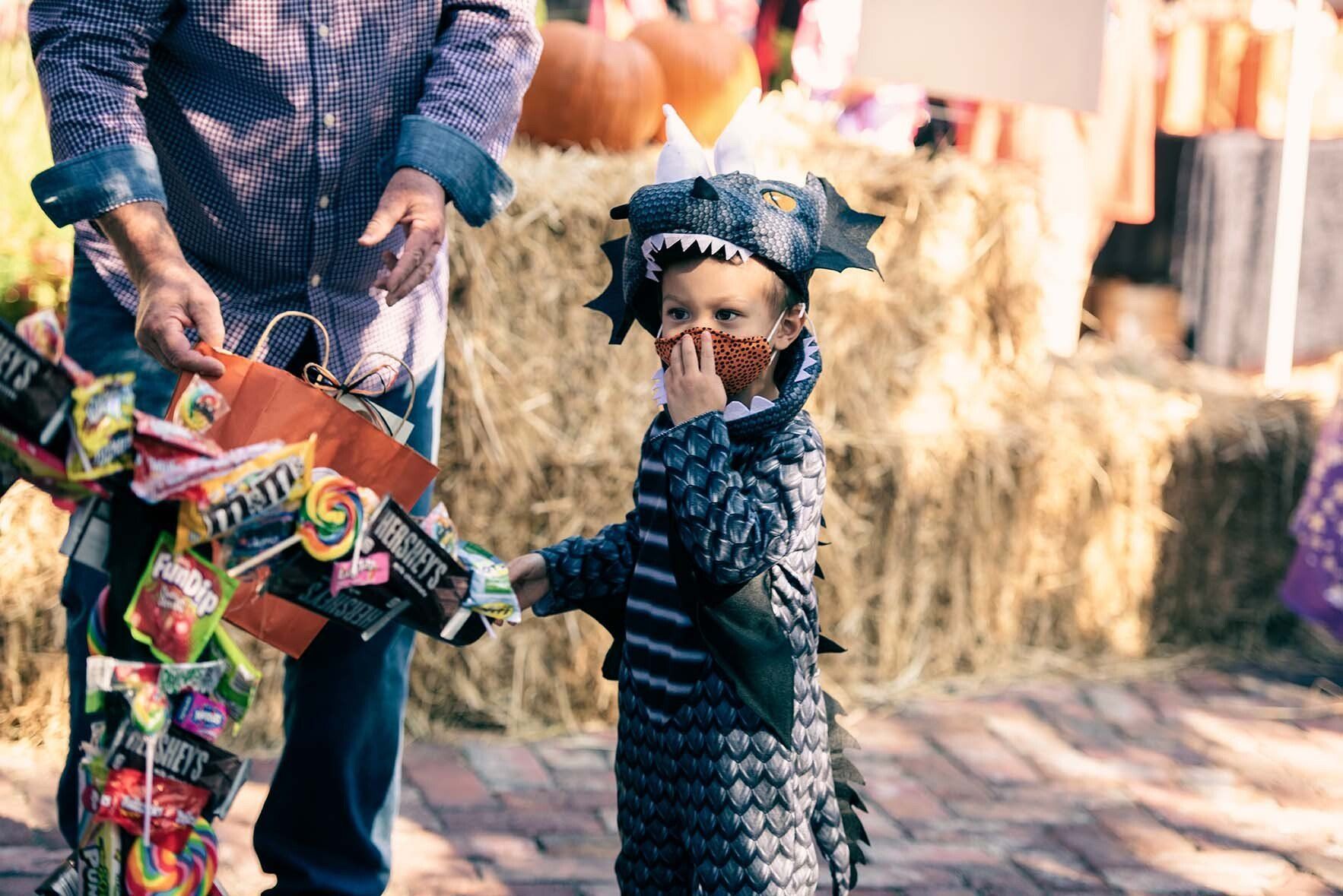 A little boy in a dragon costume is handing a bag of candy to a man.