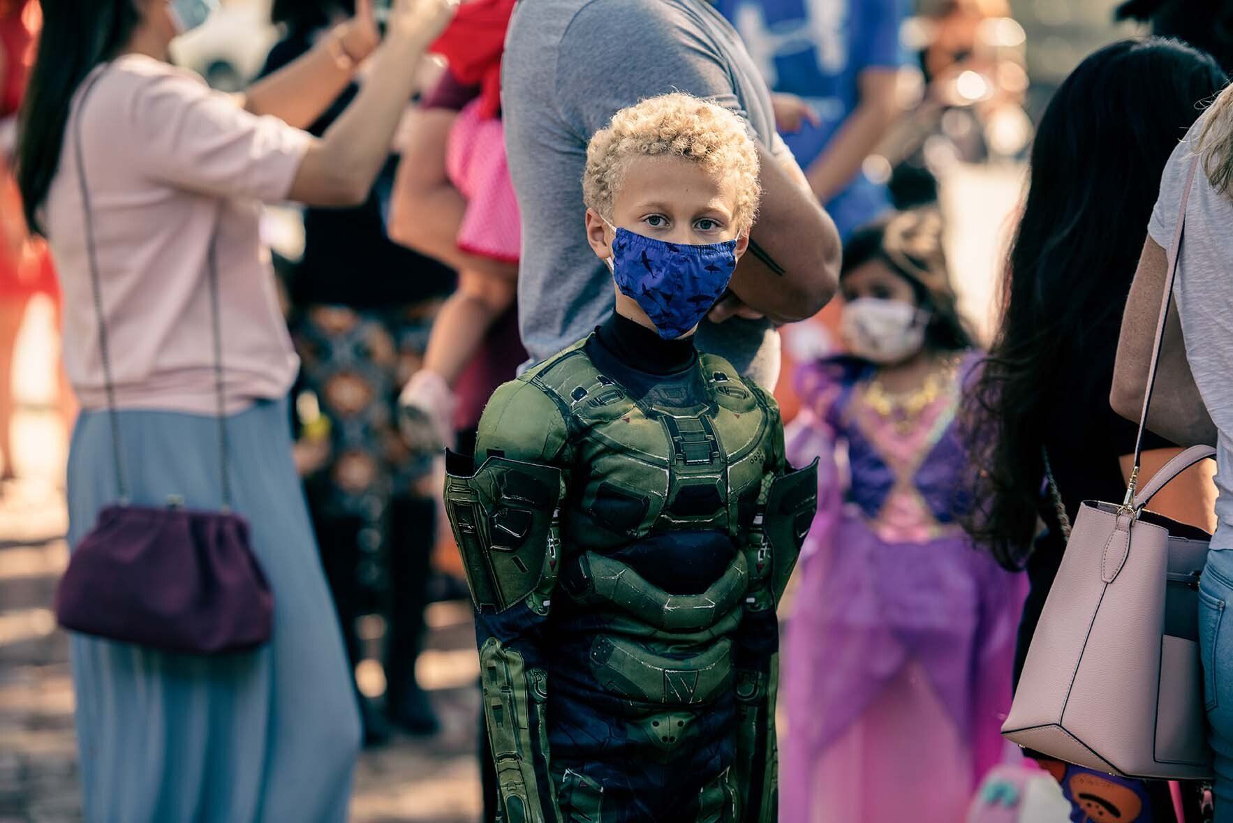 A young boy wearing a mask is standing in a crowd of people.