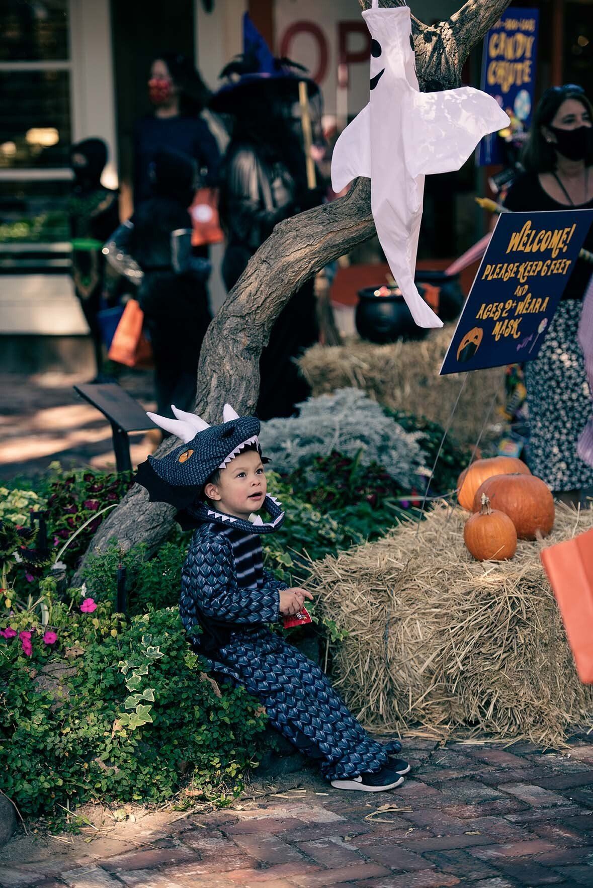A little boy in a dragon costume is sitting on a bale of hay.