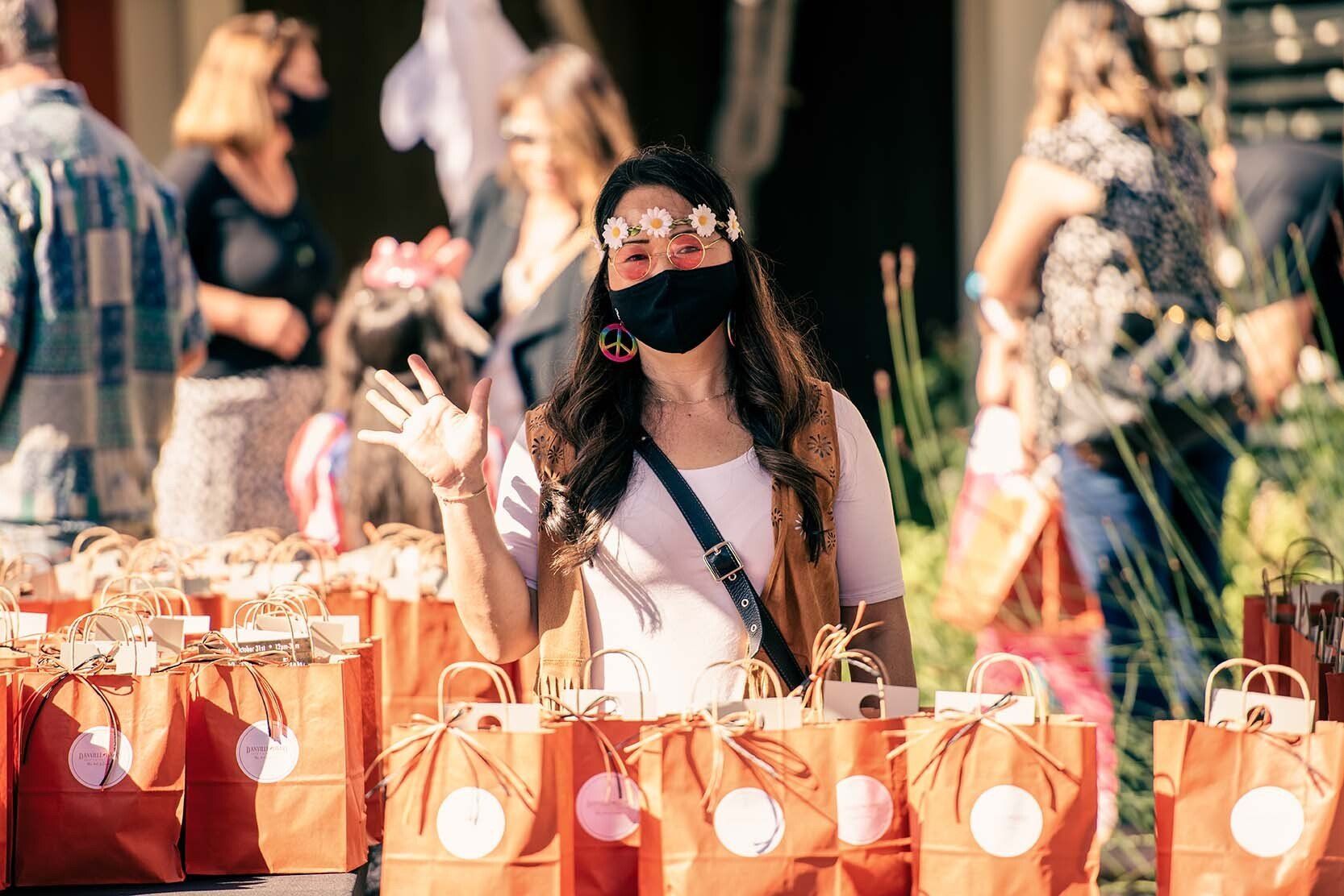 A woman wearing a mask is standing in front of a table full of bags.