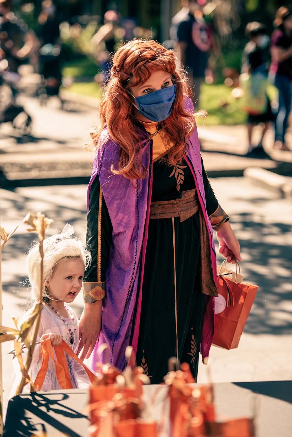 A woman dressed as anna from frozen is holding a little girl 's hand.
