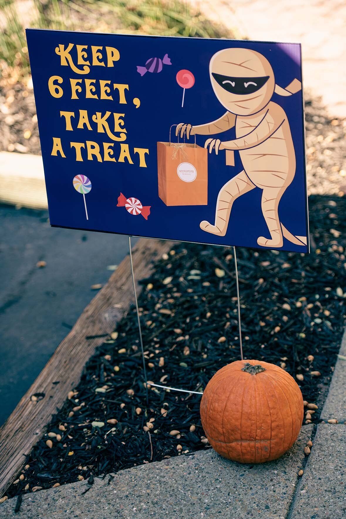 A sign that says keep 6 feet take a treat next to a pumpkin