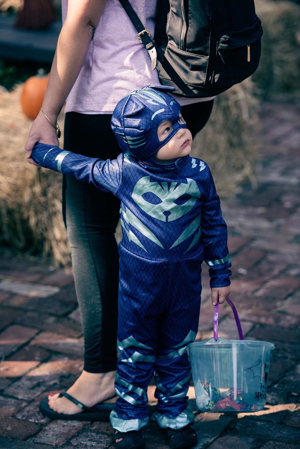 A little boy in a superhero costume is holding a woman 's hand.