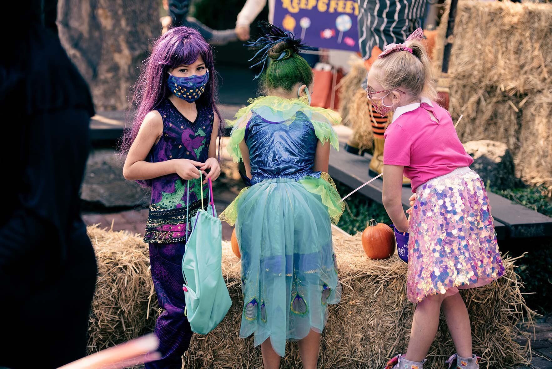 Three young girls in halloween costumes are standing next to each other on a hay bale.