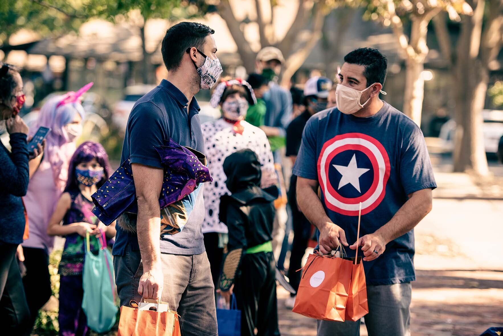 Two men wearing face masks are standing next to each other at a trick or treat event.