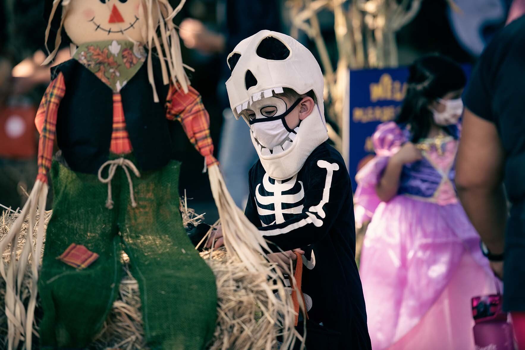 A boy in a skeleton costume is standing next to a scarecrow.