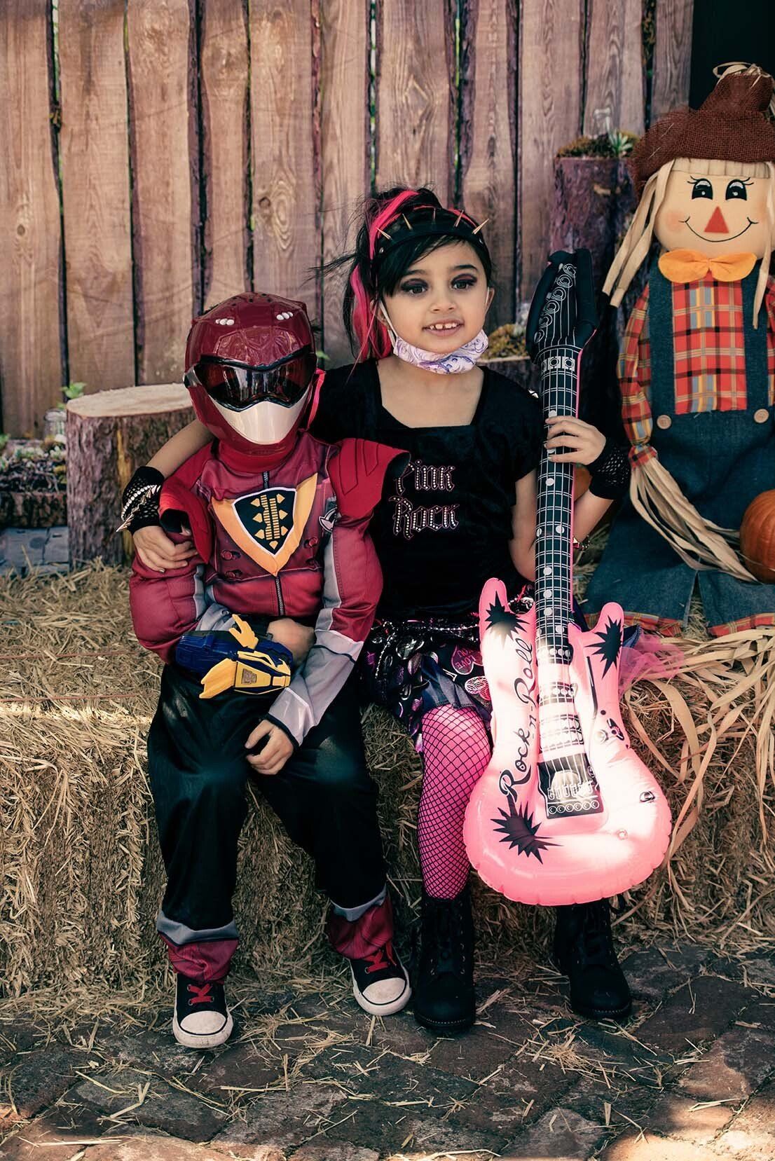 A girl is holding a pink guitar while sitting next to a boy in a superhero costume.