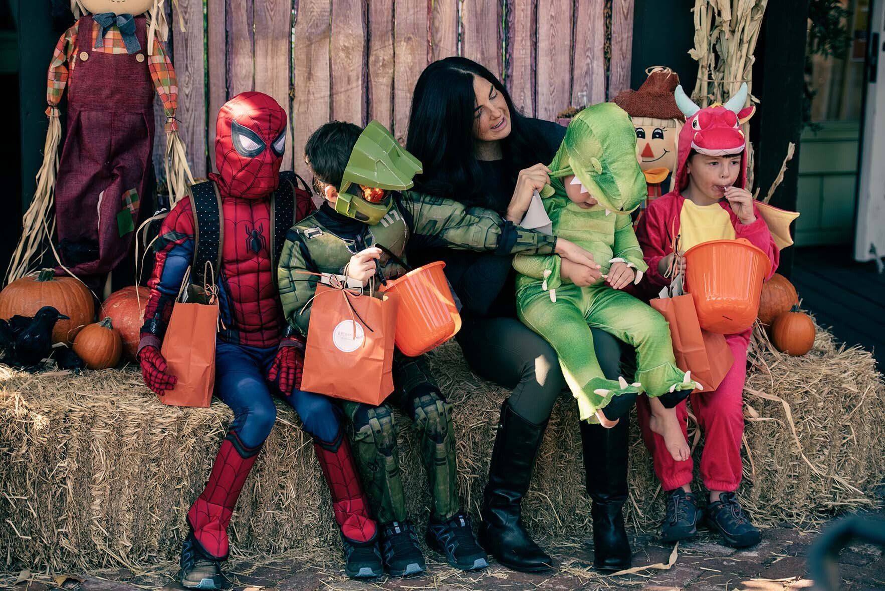 A group of children in halloween costumes are sitting on a hay bale.