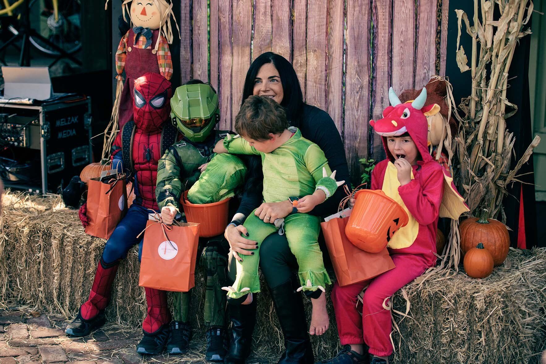 A group of children in halloween costumes are sitting on hay bales.