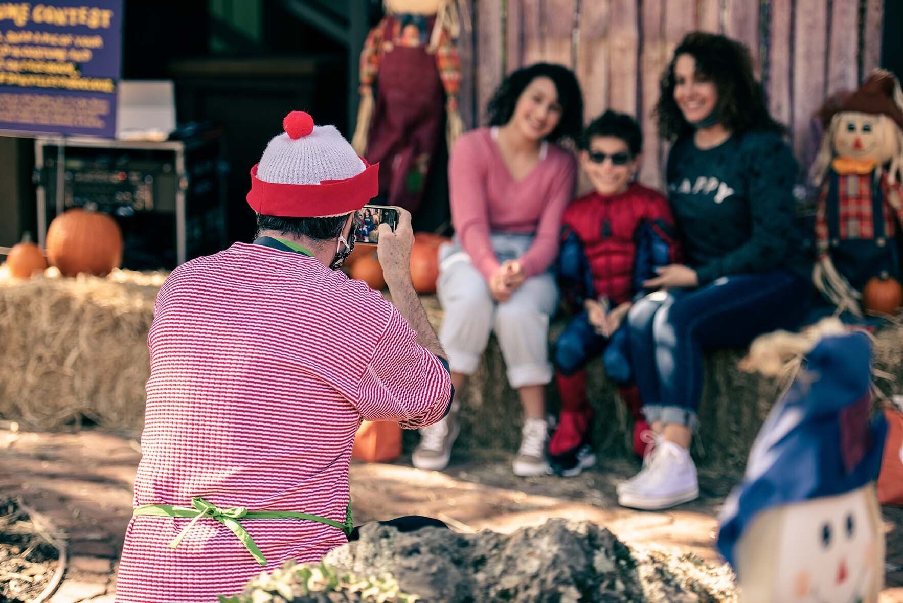 A man is taking a picture of a family at a pumpkin patch.