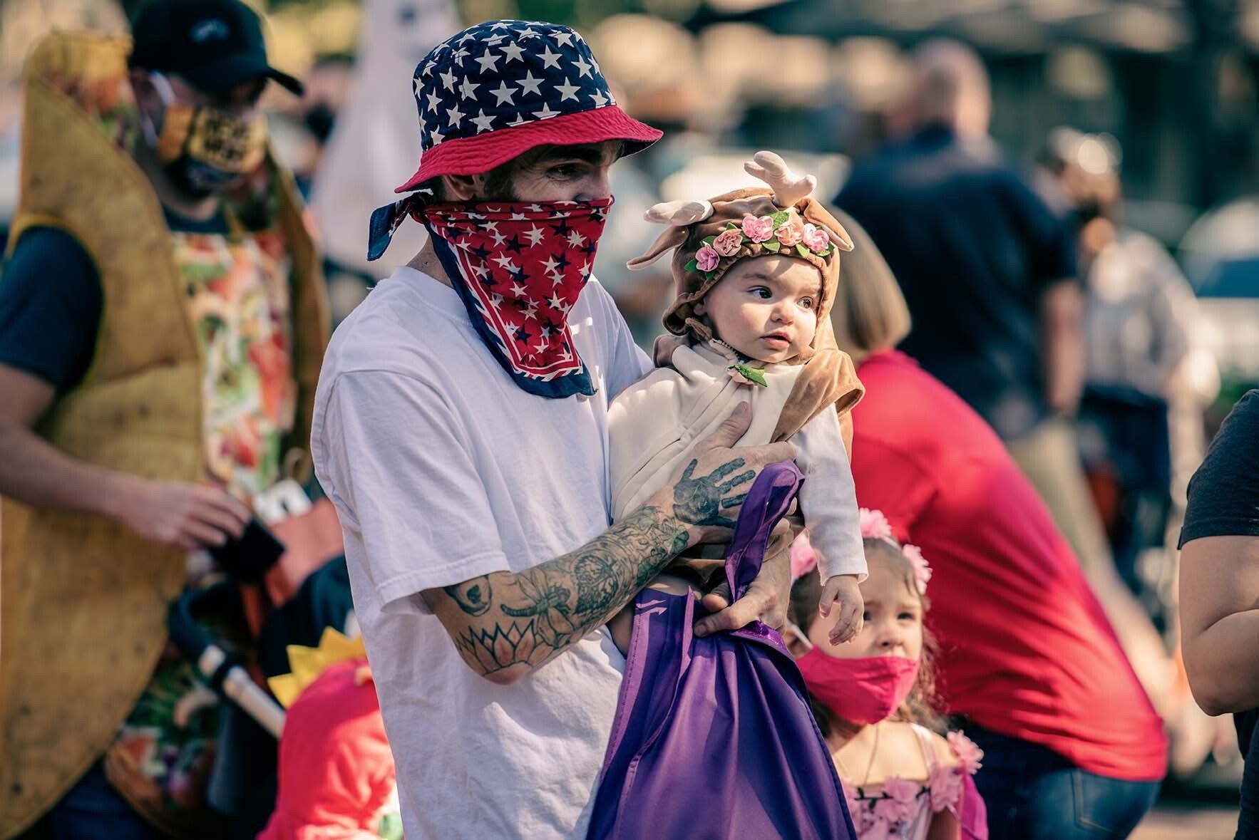 A man wearing a bandana is holding a baby in his arms.