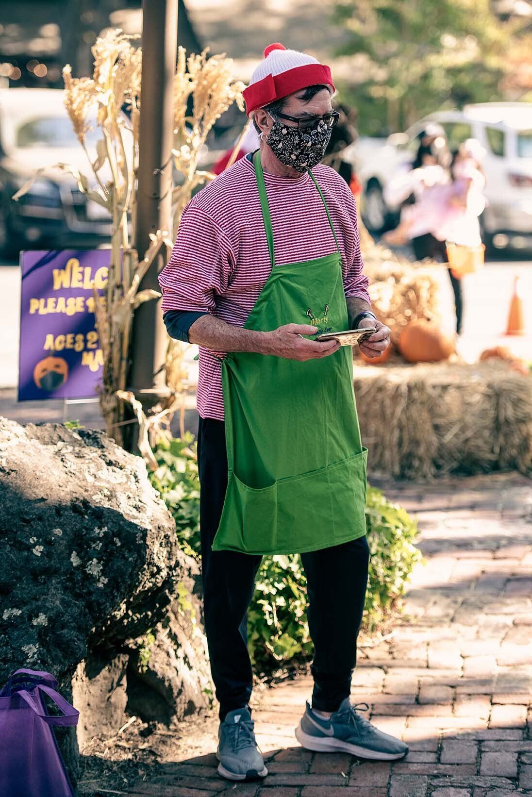 A man wearing a mask and a santa hat is standing on a sidewalk.