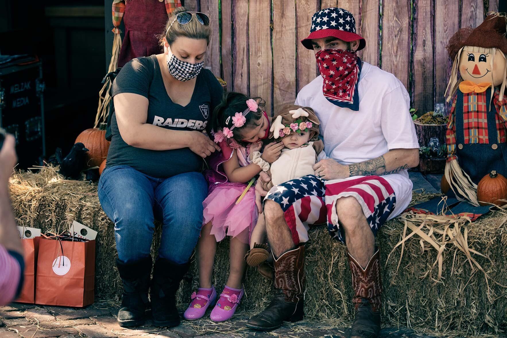 A family is sitting on a bale of hay.
