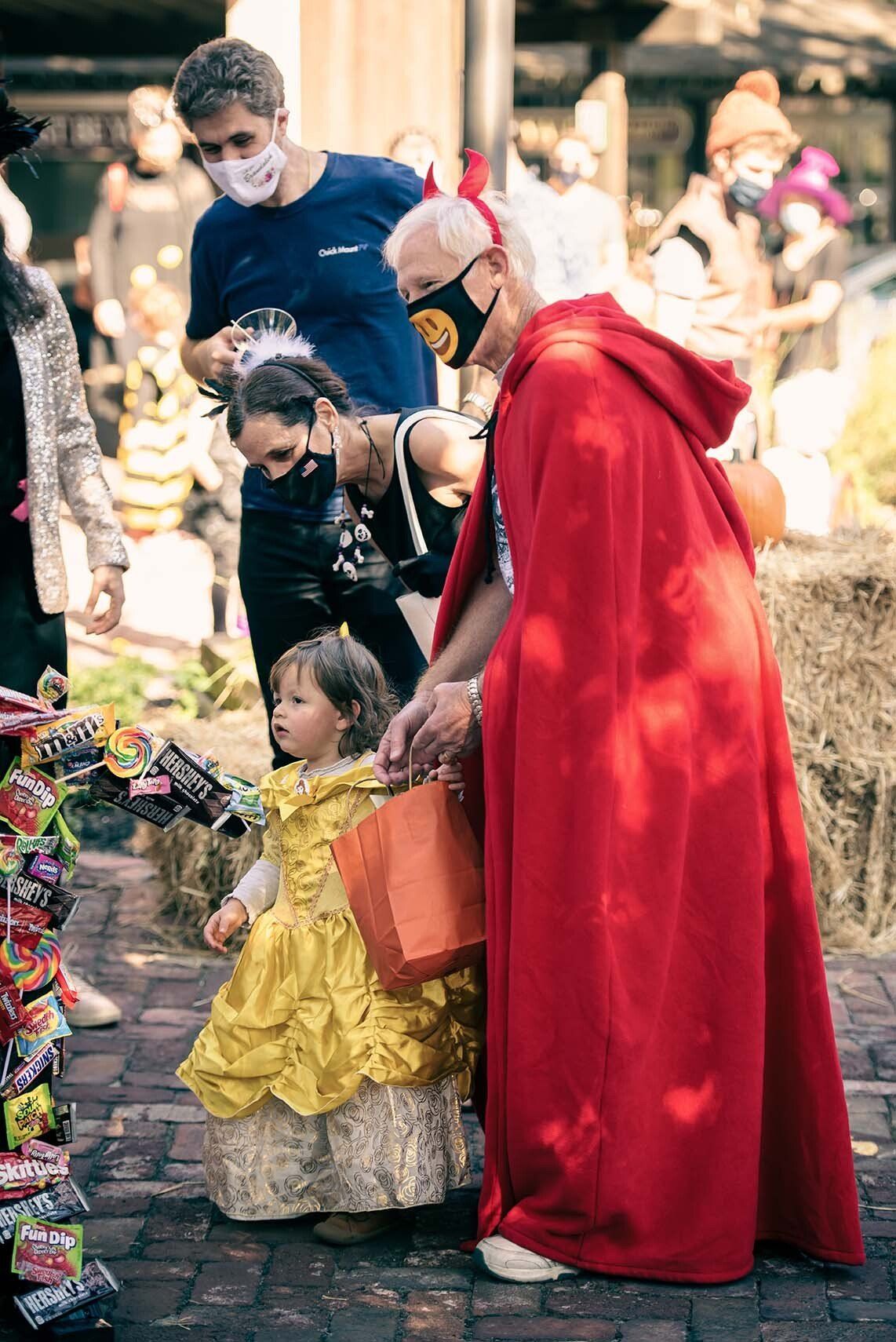 A little girl in a yellow dress is standing next to a woman in a red cape.
