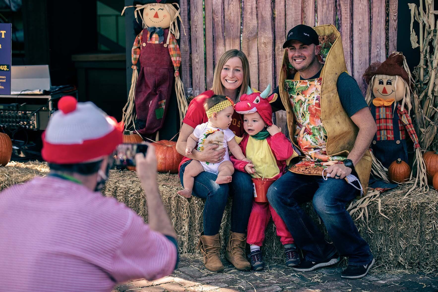 A man is taking a picture of a family sitting on hay bales.