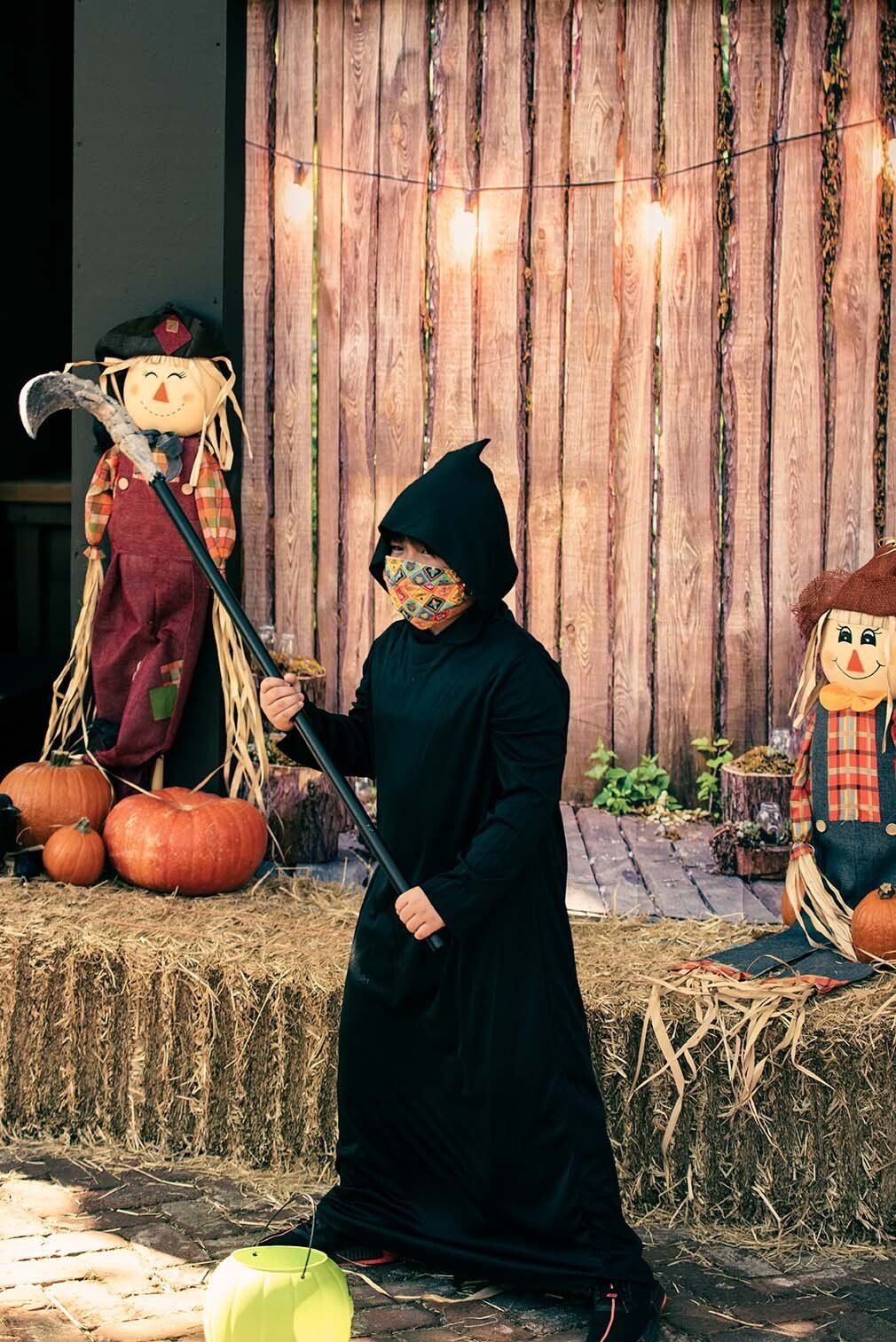 A young boy in a grim reaper costume is holding a scythe.