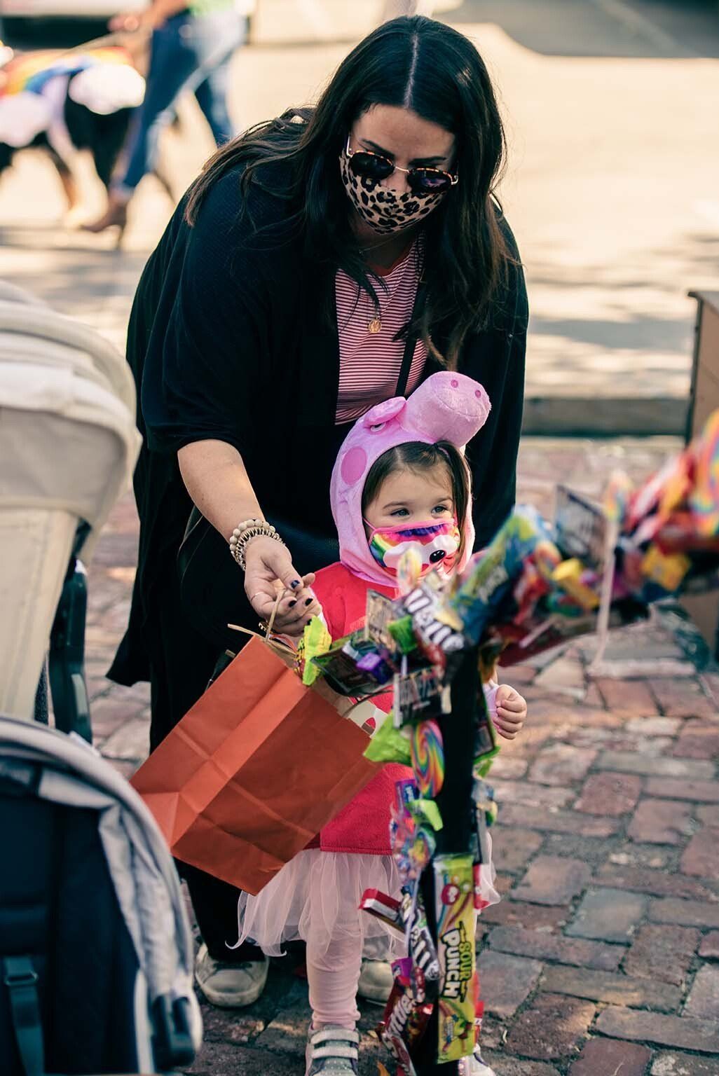 A woman is holding a bag of candy next to a little girl in a costume.