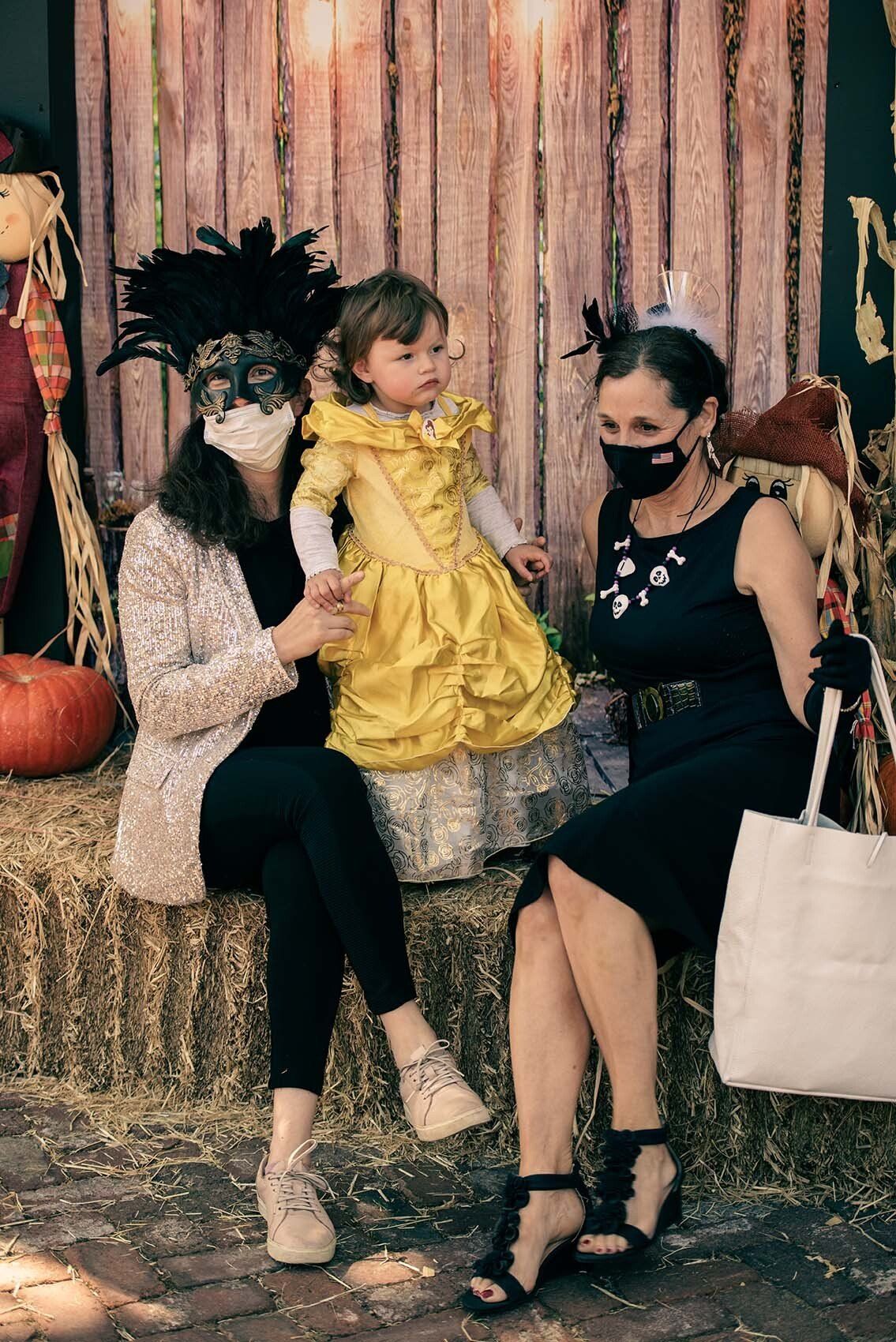 Two women and a little girl wearing masks are sitting on a hay bale.