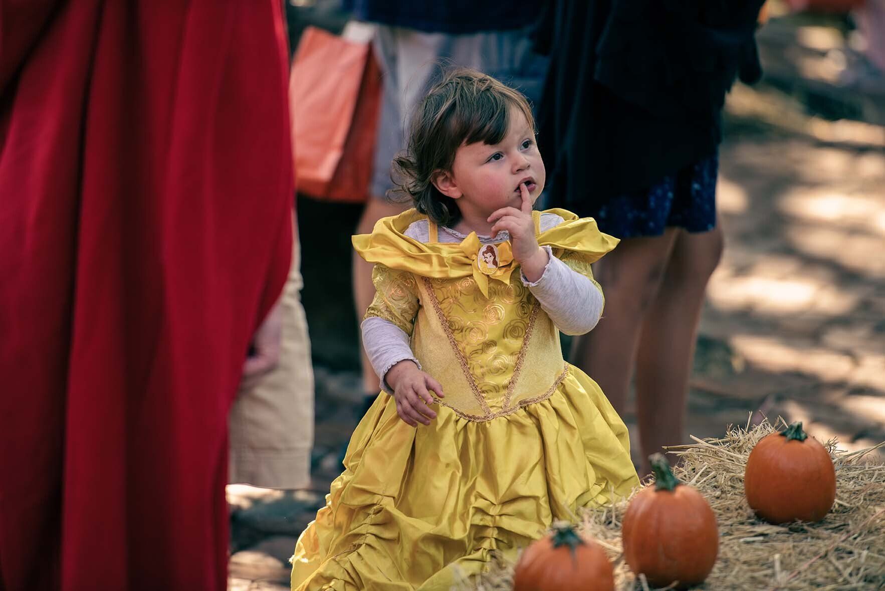 A little girl in a yellow dress is standing next to pumpkins.