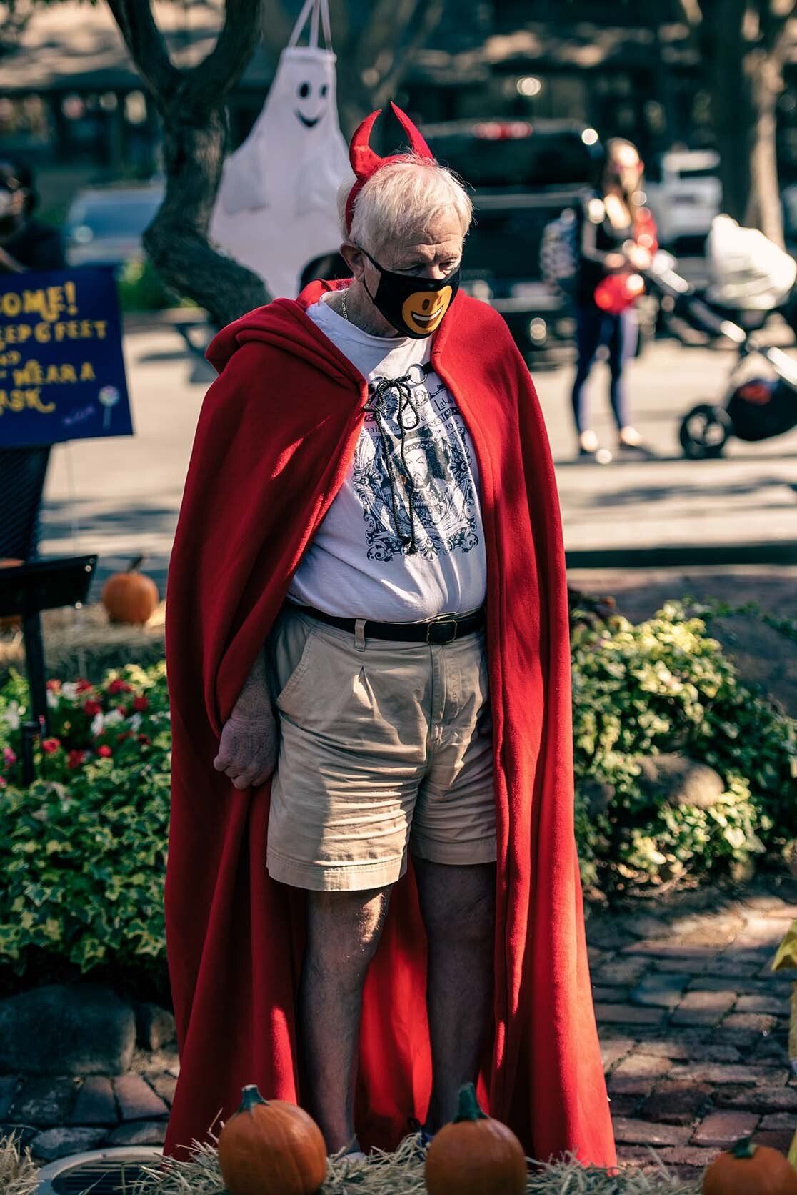 A man in a red cape and mask is standing in front of pumpkins.