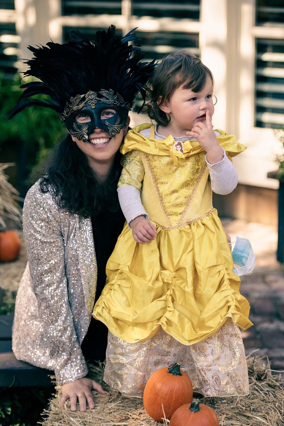 A woman wearing a mask is kneeling next to a little girl in a yellow dress.